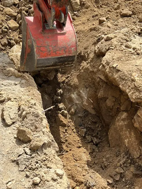 An excavator bucket digging a drainage trench