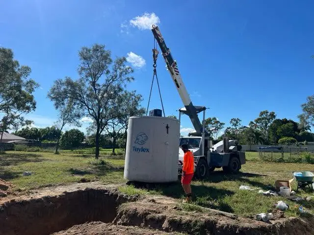 A crane lowering a concrete tank into an excavation